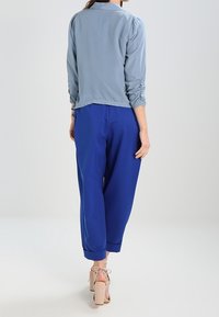 Ljust blå, långärmad blus med samlade ärmar i kombination med löst sittande, kungligt blå byxor och beige högklackade skor.