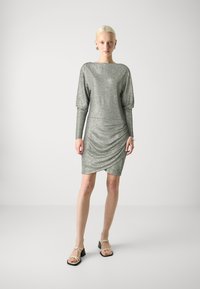 Rochie metalizată argintie cu mâneci lungi, plisate, față drapată și o siluetă ajustată. Asortată cu pantofi bej cu bretele.