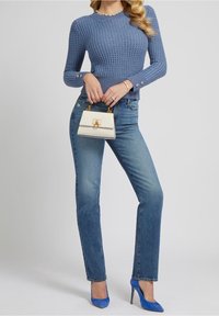 Pull en maille bleu clair avec un motif texturé, jean en denim taille haute, chaussures à talons hauts bleues, et un petit sac à main crème avec des accents dorés.