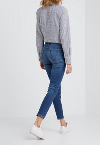 Lätt randig skjorta i blått och vitt, stoppad i mörkblå denimjeans. Hög midja med bakfickor. Bärs med vita sneakers.