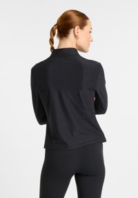 Black long-sleeve top made of textured fabric, featuring a high collar and flat seams, paired with black leggings.