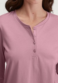 Roze langemouwen top met een ronde halslijn, vier knopen aan de voorkant en een zachte, gladde textuur. Casual ontwerp dat geschikt is voor het lagen.
