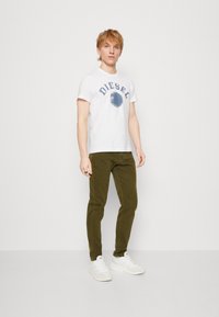 White t-shirt with blue "DIESEL" print, green slim-fit pants, and white sneakers. Simple design with a casual fit and no visible patterns.