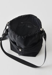 Borsa a secchiello in tessuto nero con apertura a coulisse, tasca interna con zip e tracolla regolabile. Texture liscia con pochi dettagli in metallo.