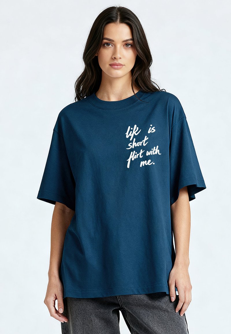 Jeune femme aux cheveux longs et foncés portant un t-shirt ample bleu marine avec un texte blanc disant « la vie est courte, flirte avec moi ».