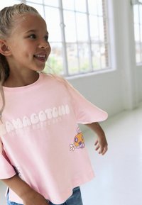 Lyserød kortærmet t-shirt med "Tamagotchi" tekst og tegneserie designs af farverige figurer, lavet af blødt bomuldsstof.