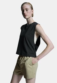 Černý bezrukávový crop top s bočními výřezy, spárovaný s béžovými šortkami s elastickým pasem a bočními kapsami. Hladká textura látky.