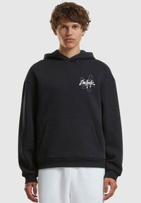 Schwarzer Kapuzenpullover aus weichem Material, mit einer Fronttasche und einem weißen Grafiklogo auf der linken Brust. Lockere Passform.