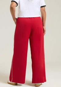 Weite Hosen in leuchtendem Rot, gefertigt aus einem glatten Material. Mit weißen Seitenstreifen und einem elastischen Bund für zusätzlichen Komfort.