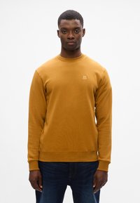 Felpa giallo senape con scollatura tonda e maniche lunghe. Presenta un piccolo logo sul petto e un tessuto morbido e strutturato.