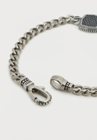 Βραχιόλι αλυσίδας από ασημί μέταλλο με περίτεχνο κούμπωμα, υφασμένους κρίκους και διακοσμητικές λεπτομέρειες στο κλείσιμο για επιπλέον αισθητική.