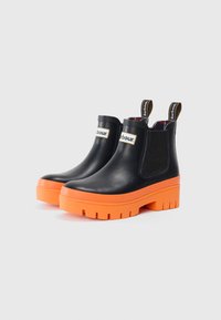 Bottines en caoutchouc noires avec des semelles en plateforme orange, des panneaux latéraux élastiques et des languettes de tirage marquées. Texture lisse avec un design durable.