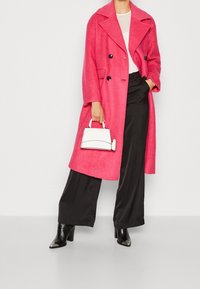 Cappotto rosa doppiopetto realizzato in tessuto testurizzato, abbinato a pantaloni neri a gamba larga e una piccola borsa bianca. Stivali neri con tacco.