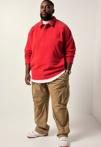 Rød fleece-pullover med krave, parret med khaki cargo-bukser. Hvid t-shirt under, komplementeret af hvid og rød sneakers.