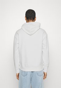 Felpa bianca in cotone con cappuccio regolabile, vestibilità ampia, polsini e orlo a coste. Indossata con jeans di denim blu chiaro.