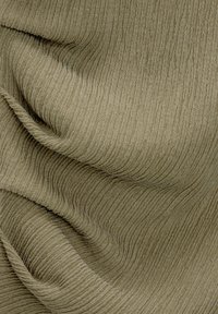 Tissu texturé en vert olive atténué, présentant des lignes verticales en relief et de douces plis drapés qui créent de la profondeur et de l'intérêt visuel.