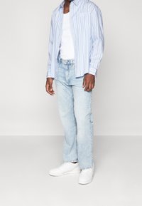 Světle modrá pruhovaná košile na knoflíky přes bílý top bez rukávů, doplněná světle modrými rovnými džíny a bílými teniskami.