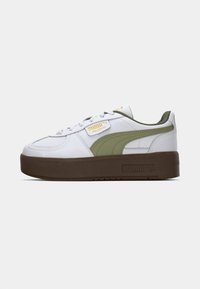 Zapatilla blanca de cuero con detalles en verde oliva, suela de goma marrón gruesa, cordones planos y una etiqueta dorada en la lengüeta.