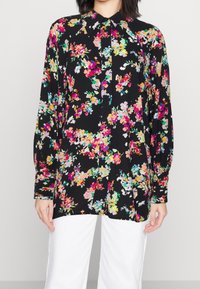 Floral blouse with black background, featuring vibrant pink, yellow, and green flowers, buttoned front, and long, puffed sleeves.