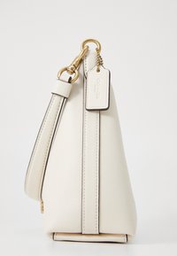 Cream leather handbag with a structured design, featuring a flat base, side zipper, and gold hardware accents, including a tag.