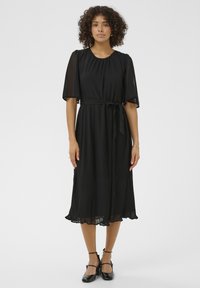 Rochie neagră cu fustă plisată, mâneci scurte din material transparent, guler rotund și o curea asortată la talie. Textura este netedă, cu o siluetă fluidă.