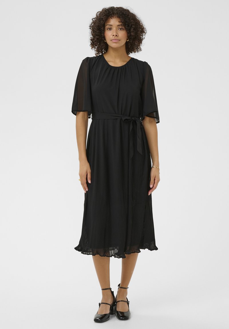 Rochie neagră cu fustă plisată, mâneci scurte din material transparent, guler rotund și o curea asortată la talie. Textura este netedă, cu o siluetă fluidă.