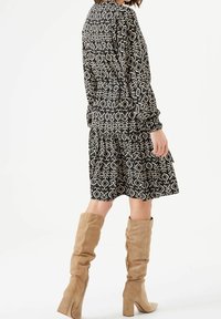 Svart och krämfärgad mönstrad klänning med långa ärmar och flerskiktad kjol, i kombination med knähöga beigea mockastövlar med klack.