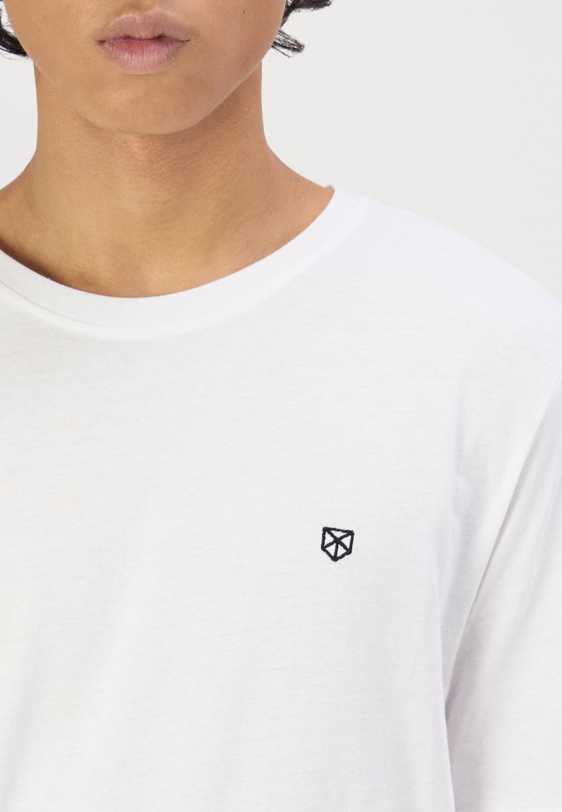 Weißes Kurzarm-T-Shirt aus weicher Baumwolle mit kleinem schwarzem geometrischem Logo auf der Brust, Rundhalsausschnitt und glatter Textur.