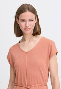 Rustkleurige jurk van zachte stof, met een V-halslijn, korte mouwen en een gestrikte taille voor een aansluitende pasvorm.