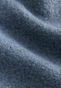 Material texturat albastru cu suprafață pufoasă, prezentând un model moale, ridicat. Materialul pare cald și primitor.