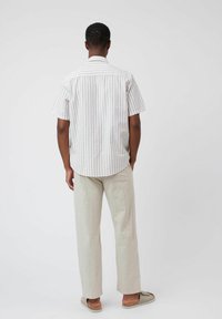 Chemise à manches courtes rayée en beige clair et blanc, associée à un pantalon large de couleur claire. La chemise a un col et un ourlet arrondi.
