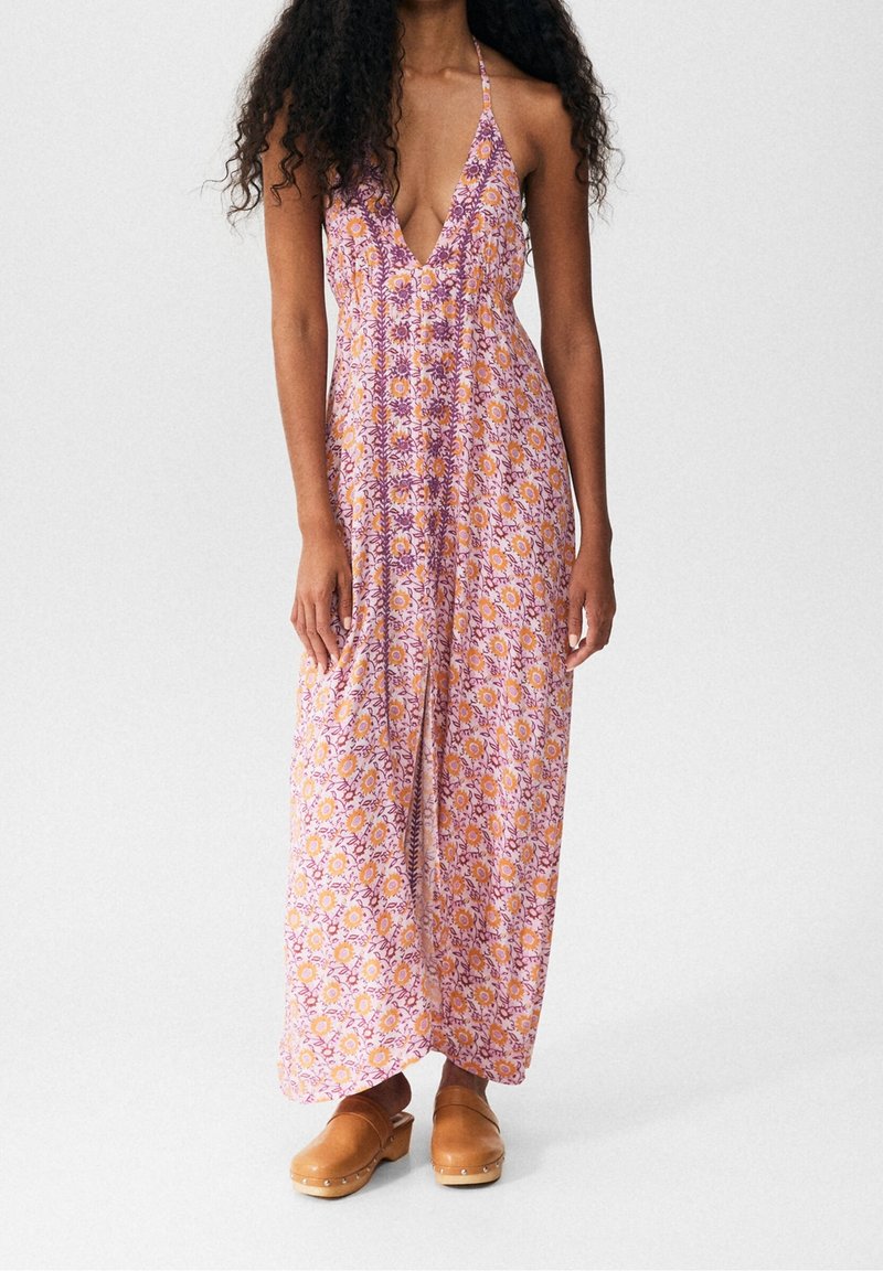 Vestido maxi en rosa con estampados florales en naranja y morado. Presenta un escote en V profundo y tirantes tipo halter, fabricado en un tejido ligero.