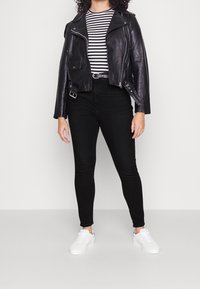 Chaqueta de cuero negra de motorista con bolsillos con cremallera, camiseta de rayas en blanco y negro, jeans skinny negros y zapatillas blancas.