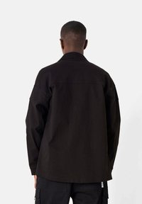 Black long-sleeve shirt with a relaxed fit, a collar, and a straight hem. Features a smooth texture and minimal stitching details.