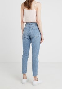 Světlé modré džíny s vysokým pasem, k tapered nohavicím, s třepeným lemem a dvěma zadními kapsami, kombinované s jednoduchou růžovou topem a bílými teniskami.