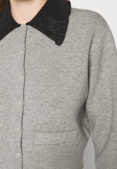 Pilkas kardiganas su tekstūruotu juodu apykakle, apvaliais mygtukais ir dviem priekinių kišenių, pagamintas iš minkštos mezginio medžiagos.