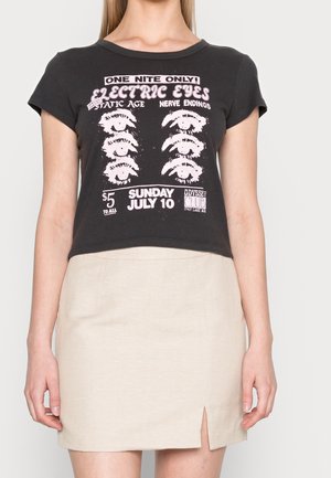 Black cropped t-shirt featuring a graphic design with pink text and eye illustrations. Paired with a beige skirt with a front slit.