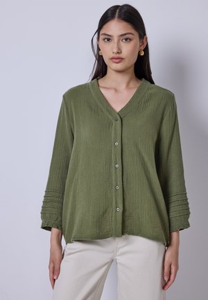 Blusa verde oliva con bottoni in tessuto testurizzato, scollo a V, maniche a tre quarti e dettagli delle maniche plissettate. Chiusura semplice con bottoni.
