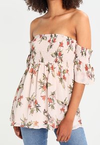 Top floreale leggero rosa pallido con scollo off-the-shoulder, corpetto arricciato, maniche a volant e motivi di fiori multicolori. Vestibilità casual.