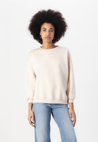 Helle beige Sweatshirt mit strukturiertem Finish, Rundhalsausschnitt und überschnittenen Schultern. Verfügt über gerippte Bündchen und Saum. Kombiniert mit hellblauen Jeans.
