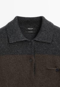 Sweter polo z kaszmiru w ciemnoszarym i brązowym kolorze. Posiada kołnierzyk, trzy guziki oraz kieszeń z guzikiem na klatce piersiowej.