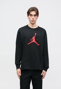 Μαύρη μακρυμάνικη μπλούζα από βαμβάκι, με κόκκινο λογότυπο Jumpman στο μπροστινό μέρος. Ριμπ κολλάρο και μανσέτες, σχεδίαση χαλαρής εφαρμογής.