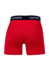 Piros boxer alsónadrág fekete derékkal, rajta a "LACOSTE" logóval. Puha anyagból készült, testhezálló fazonban, további minták nélkül.