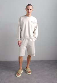 Helebeez sweatshirt koos soonikute ja sobivate lühikestega. Kanda tan värvi sussidega, millel on sile tekstuur ja minimaalne disain.