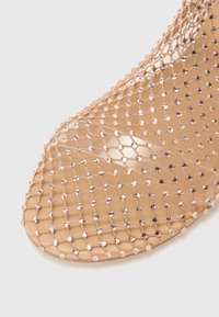 Chaussure à bout ouvert avec un design en résille coloris nude, ornée de strass brillants, d'une texture lisse et d'une forme arrondie.