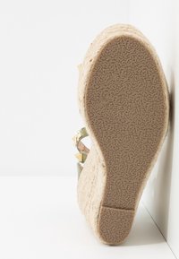 Vue de la semelle d'une sandale compensée espadrille beige avec semelle extérieure en caoutchouc texturé et talon plateforme en jute tissé.