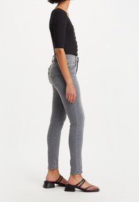 Jeans ajustados de tiro alto en gris con una textura suave, combinados con sandalias negras con tiras y un tacón grueso.
