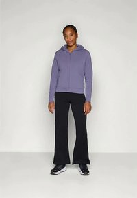 Varianta fialovej mikiny na zips s kapucňou, skombinovaná s čiernymi rozšírenými nohavicami a čiernymi teniskami. Hladká tkanina s voľným strihom. Jednoduchý dizajn bez vzorov.