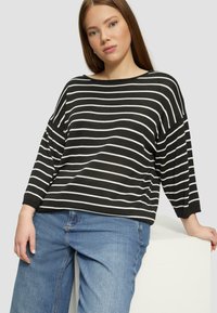 Haut à rayures noir et blanc à manches longues avec un col rond large et une coupe décontractée, associé à un jean en denim bleu clair.