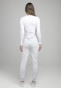 Bílý dlouhý rukáv top a světle šedé tepláky s elastickým pasem, přiléhavými manžetami a bočními kapsami; doplněné bílými sportovními botami.